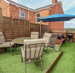 An outdoor patio area with chairs around a glass table a blue umbrella a grill and a sofa at Corner House in Cinderford