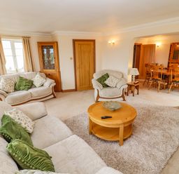 A living room with sofas and green cushions and a wooden coffee table leading to a dining area at Corner House in Cinderford