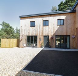 A modern wood clad house with black framed windows and doors with gravel and asphalt driveway at Stag Cottage in Lytchett Matravers