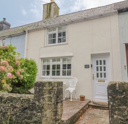 A front view of a cream colored house with white door and windows and a small patio with white chairs and a table at Ty Coed in Beaumaris