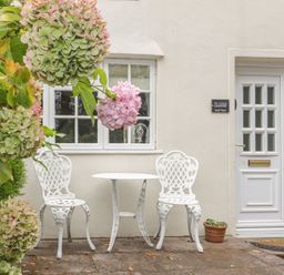 A small outdoor patio with two white metal chairs and a round table near a white door and window at Ty Coed in Beaumaris