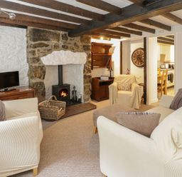 A living room with white sofas a stone fireplace a TV and a view into a kitchen at Ty Coed in Beaumaris