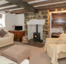 A living room with two armchairs a footstool a wood stove and wooden beams on the ceiling at Ty Coed in Beaumaris