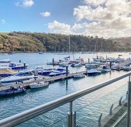 Boats docked at a marina with a glass railing in the foreground and wooded hills in the background at 15 Dart Marina in Dartmouth