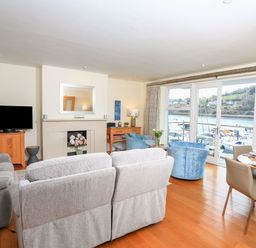 A living room with sofas a TV and a dining table with a marina view at 15 Dart Marina in Dartmouth