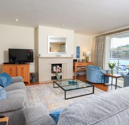 A living room with grey sofas a glass coffee table a fireplace TV and windows overlooking a marina at 15 Dart Marina in Dartmouth