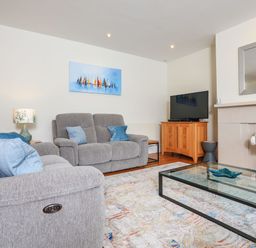 A living room with grey sofas a glass coffee table a TV on a wooden stand and a fireplace with flowers at 15 Dart Marina in Dartmouth