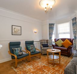 A living room with chairs a small table and window curtains at Apple Tree House in Hunstanton