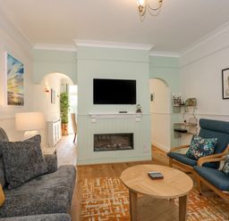 A living room with sofa and armchairs facing a fireplace and wall mounted TV at Apple Tree House in Hunstanton