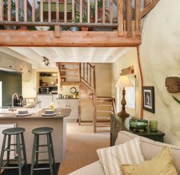 A kitchen and living area with wooden stairs plants and a sofa at The Byre in Monkleigh near Great Torrington
