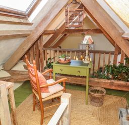 A loft area with a wooden chair by a green table with plants and a lamp at The Byre in Monkleigh near Great Torrington