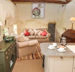 A living room with sofas and a wooden cabinet next to a kitchen island with cups and a coffee press at The Byre in Monkleigh near Great Torrington