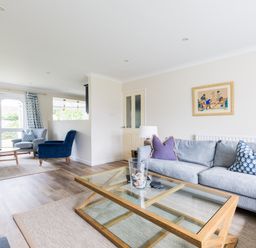 A living room with a glass coffee table a grey sofa with pillows two blue armchairs wooden floors and large windows at Silverdale in Rock