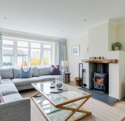A living room with a large gray sectional sofa and a glass coffee table in front of a fireplace with a wood stove at Silverdale in Rock