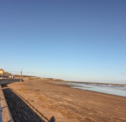 A sandy beach with a metal railing along a paved walkway and buildings in the distance at The Lazy Seal in Spittal