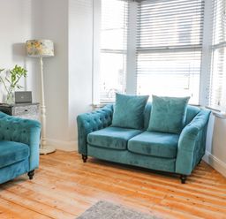 A living room with two teal sofas a floor lamp and a side table with flowers at The Lazy Seal in Spittal