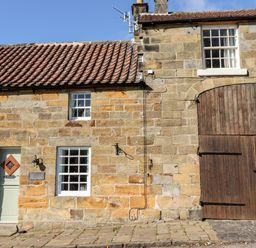 Stone building with tiled roof green door windows and large wooden barn door at Michaelmass Cottage in Castleton