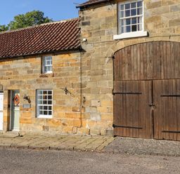 Exterior of a stone building with tiled roof two doors and large wooden barn door at Michaelmass Cottage in Castleton