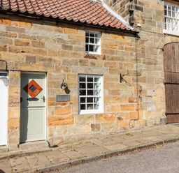 Stone building facade with two windows two doors and wooden barn doors at Michaelmass Cottage in Castleton