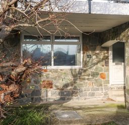 The exterior of a stone house with a white door a window and a tree in front at 5 Ger Y Nant in Llanbedrog