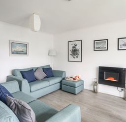 A living room with blue sofas cushions an ottoman wall art and a wall-mounted electric fireplace at 5 Ger Y Nant in Llanbedrog