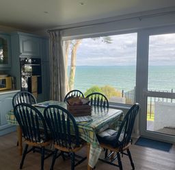 A kitchen with blue cabinets a dining table with six chairs and a large window overlooking the sea at Rocklea Seaside Cottage in Newcastle County Down