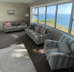 A living room with sofas and armchair facing large windows with a sea view at Rocklea Seaside Cottage in Newcastle County Down