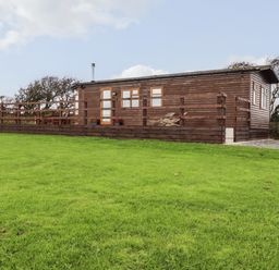 A wooden cabin with a raised deck and railing on a grassy field at Sycamore Lodge in Porkellis near Helston