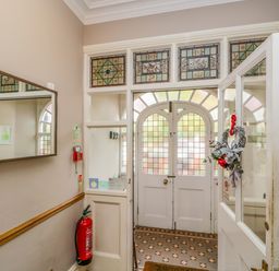 An entrance hall with a stained glass front door a fire extinguisher a wall mirror and a wreath on the door at Hollywood in Windermere