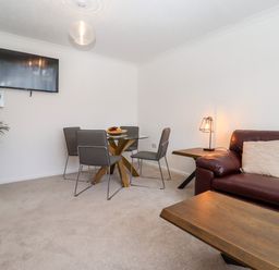 A dining area with a round glass table and four chairs next to a living room with a brown leather sofa and a wooden coffee table at 3 Granbrook Lane in Mickleton Gloucestershire