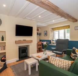 A living room with a green sofa a blue armchair a coffee table a wall-mounted television and a window with cushions at Holly Cottage in West Coker