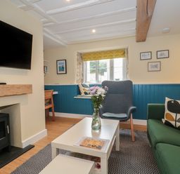 A living room with a green sofa a gray armchair a white coffee table with flowers and a fireplace at Holly Cottage in West Coker