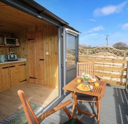 A small wooden kitchen inside with a countertop and appliances next to a wooden deck with a table set for breakfast at Claerwen Nant-glas near Rhayader