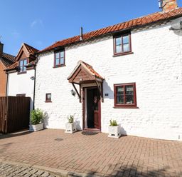 A white stone house with red roof tiles and brown window frames with a paved driveway at Chalk Cottage in Feltwell
