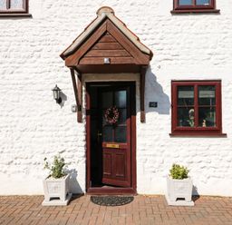 The front entrance of a white house with a brown door and two potted plants on either side at Chalk Cottage in Feltwell