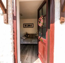 An open wooden door with a floral wreath leads to a room with a grey sofa and framed pictures on the wall at Chalk Cottage in Feltwell