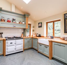 A kitchen with wooden countertops green cabinets a white stove a farmhouse sink and windows showing trees at Eagle Farmhouse in Glenridding