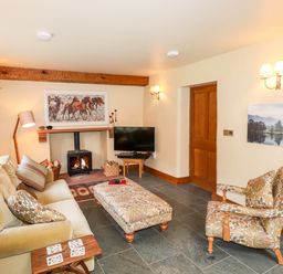 A living room with a sofa a patterned armchair a fireplace and a television at Eagle Farmhouse in Glenridding