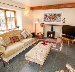A living room with a sofa and ottoman near a fireplace with a wood stove and a television at Eagle Farmhouse in Glenridding