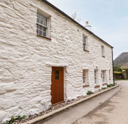 A white stone cottage with brown wooden door and multiple windows along a narrow road at Eagle Farmhouse in Glenridding