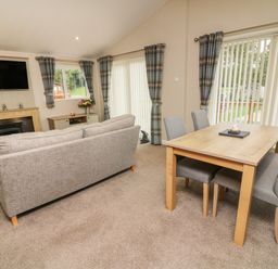 A living room with a grey sofa a wooden dining table with four chairs a fireplace and windows with plaid curtains at The Warren in Hellifield