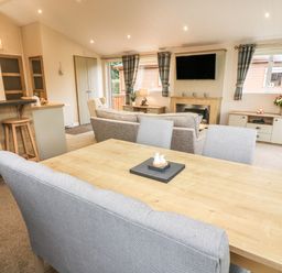 A dining table with chairs and a living room with sofas a fireplace and a wall-mounted TV at The Warren in Hellifield