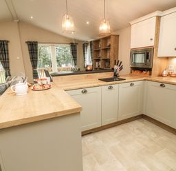 A kitchen with wooden countertops white cabinets a microwave a knife set and a teapot with treats on the counter at The Warren in Hellifield