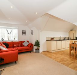 A living room with an orange sectional sofa and a small black side table next to a kitchen area with light wood cabinets and dining table at Bayview Loft in Weymouth
