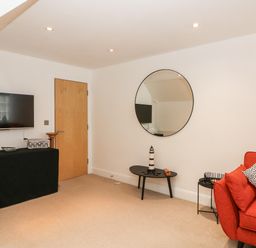 A living room with a red sofa, round mirror on the wall, black table with lighthouse decoration and a TV mounted on the wall at Bayview Loft in Weymouth