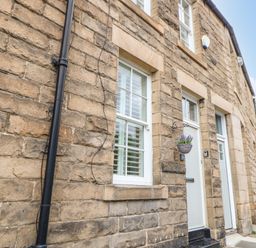 Stone exterior wall with two white doors and windows and a hanging basket on a street at Toll House in Corbridge
