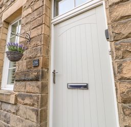 An exterior view of a stone house with a white door and window a hanging basket with purple flowers and a house number 29 at Toll House in Corbridge