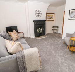 A living room with a grey sofa and cushions a black fireplace with flowers a grey armchair a small yellow table and a TV at Toll House in Corbridge
