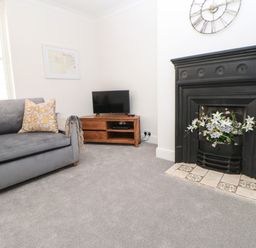 A living room with a gray sofa a wooden TV stand with a television and a black fireplace with flowers at Toll House in Corbridge