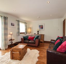 A living room with two brown leather sofas with cushions a wooden chest on a rug and curtains at The Hideout in Portree